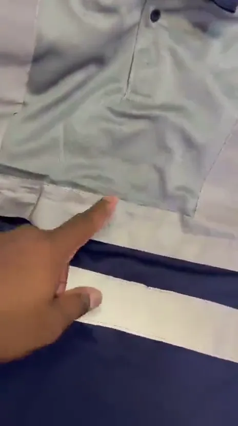 Close-up of a grey golf shirt and a navy garment with a silver reflective band, with a hand pointing to the reflective strip